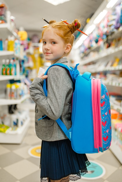 Petite écolière avec sac à dos en papeterie. Enfant de sexe féminin achetant des fournitures de bureau en magasin, écolier en supermarché