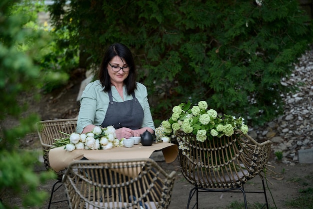 Petite entreprise belle fleuriste senior sur la terrasse verte fait un bouquet et prend une commande par téléphone