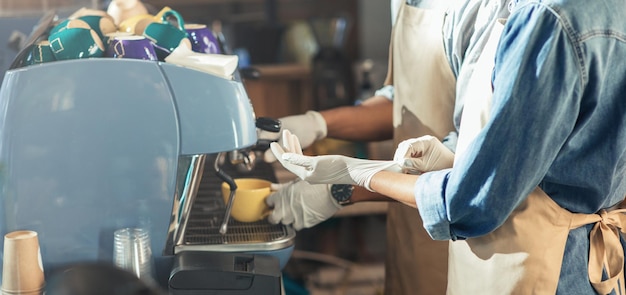 Petite entreprise familiale et distanciation sociale, pendant l'épidémie de covid-19. Jeune femme afro-américaine en tablier mettant des gants en caoutchouc, un homme fait un verre sur une machine à café professionnelle, une éruption solaire