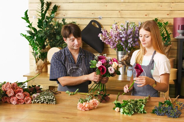 Petite entreprise. Fleuristes mâles et femelles faisant un bouquet de roses dans un magasin de fleurs. Propriétaire de l'homme et assistante dans la boutique de fleurs, faire des décorations et des arrangements Livraison de fleurs, création de commande