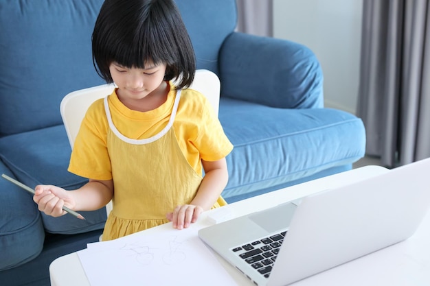 Une petite étudiante asiatique étudie en ligne à l'aide d'un ordinateur portable à la maison