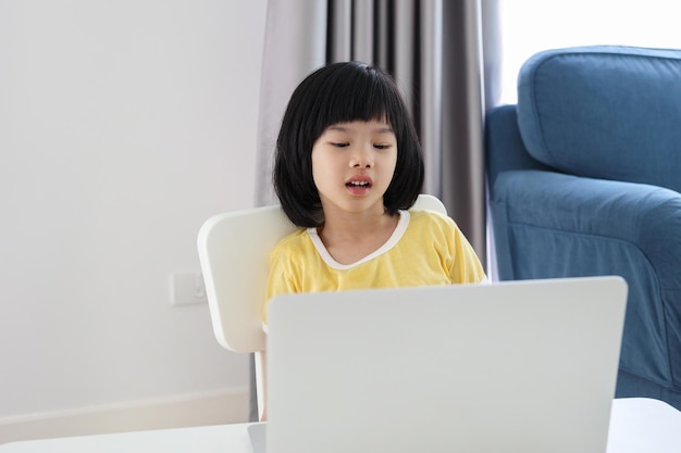 Une petite étudiante asiatique étudie en ligne à l'aide d'un ordinateur portable à la maison