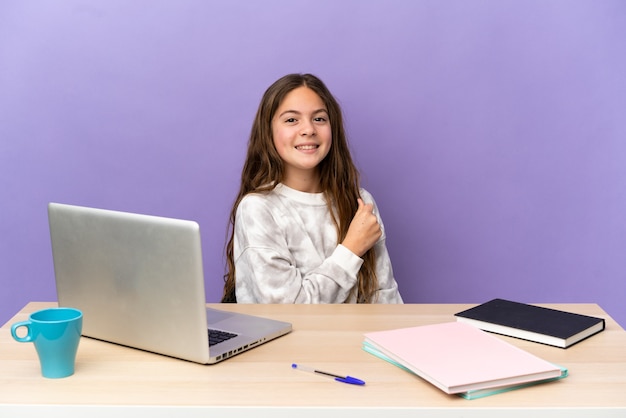 Petite étudiante dans un lieu de travail avec un ordinateur portable isolé sur fond violet célébrant une victoire