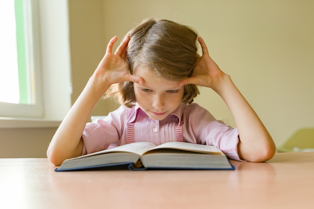 Petite étudiante est assise à un bureau avec un livre