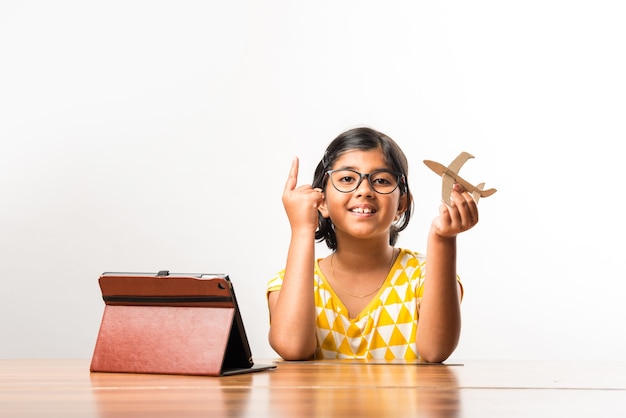 Petite étudiante indienne fabriquant ou mesurant des ailes d'avion en papier ou d'avion, faisant un projet scolaire ou apprenant les sciences avec un didacticiel en ligne