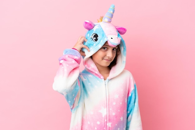 Petite femme caucasienne portant un pyjama licorne isolé sur fond rose ayant des doutes