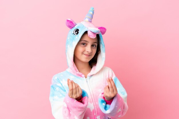 Petite femme caucasienne portant un pyjama licorne isolé sur fond rose faisant un geste d'argent