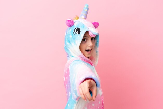 Petite femme caucasienne portant un pyjama licorne isolé sur fond rose pointant vers l'avant avec une expression heureuse