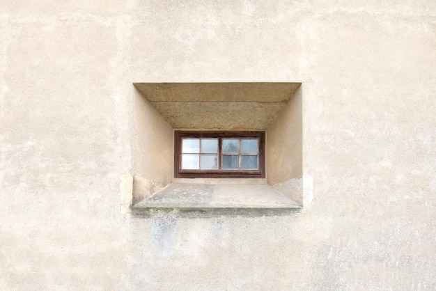 Petite fenêtre étroite avec cadre marron sur fond de mur en pierre blanche