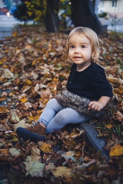 Une petite fille de 1,5 ans est debout et souriante. L'enfant jette des feuilles. Fille gaie dans la forêt d'automne