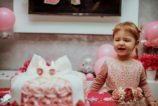 Petite fille de 2 ans en robe rose avec son premier gâteau d'anniversaire, carte de joyeux anniversaire, une jolie petite fille fête son premier anniversaire entourée de cadeaux