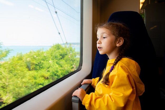 Une petite fille de 6-7 ans regarde par la fenêtre d'un train à la mer.