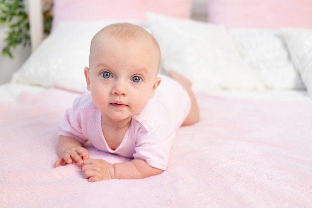 Petite fille de 6 mois rampant sur un lit blanc et rose à la maison