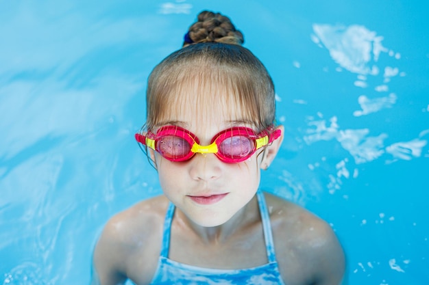 Une petite fille de 7 ans nage dans la piscine La fille est assise dans la piscine avec des lunettes de natation