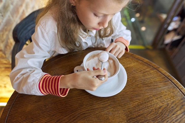 Photo petite fille de 9, 10 ans avec une tasse de chocolat chaud assis dans un café à table, espace pour copie