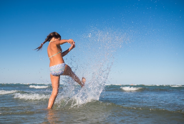 Petite fille active drôle éclaboussant dans la mer bruyante