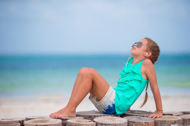 Petite fille adorable, écoutant de la musique sur un casque sur la plage