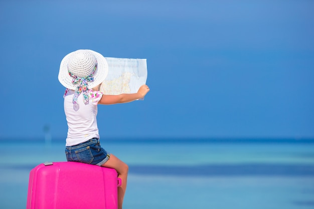 Petite fille adorable avec gros bagages et carte d&#39;île sur la plage blanche