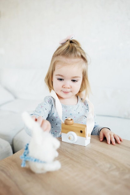 Petite fille adorable jouant avec un appareil photo jouet en bois et un jouet lapin moelleux