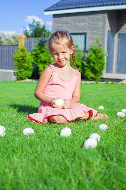 Petite fille adorable jouant avec des oeufs de Pâques blancs dans la cour