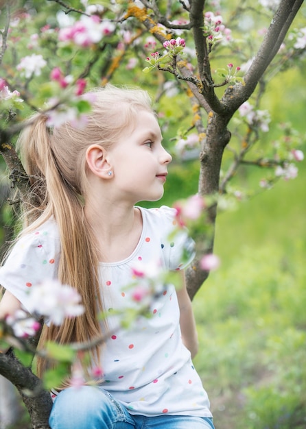 Petite fille adorable s'asseyant sur l'arbre de floraison dans le jardin de pomme