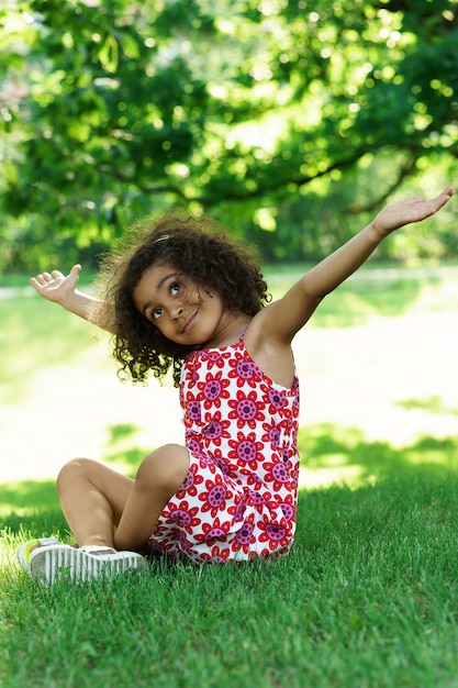 Petite fille africaine assise sur une herbe dans un parc de la ville