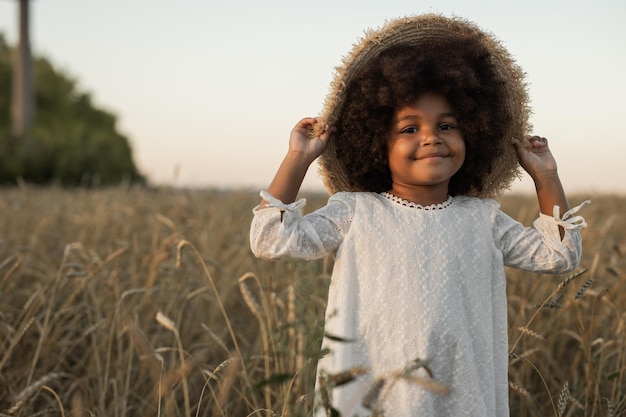 une petite fille africaine heureuse dans un chapeau en promenade dans un champ d'été