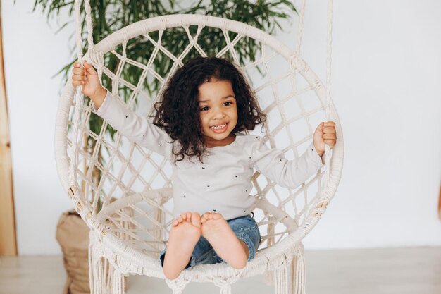 Petite fille afro-américaine dans une chaise en osier accrochée dans le salon