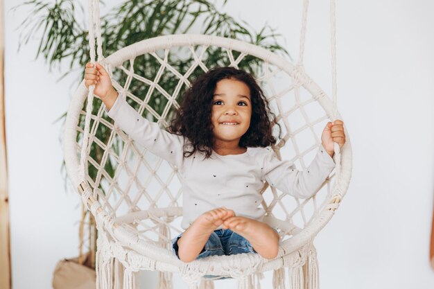 Petite fille afro-américaine dans une chaise en osier accrochée dans le salon