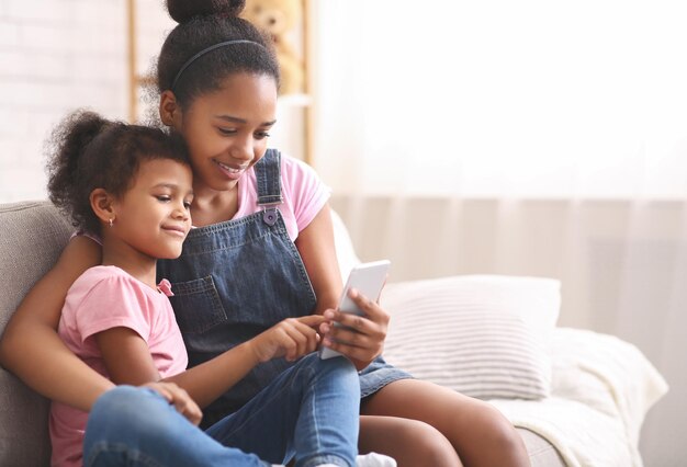 Petite fille afro-américaine jouant sur le téléphone portable de sa soeur