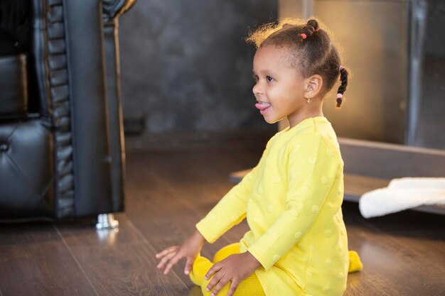 Une petite fille afro-américaine vêtue d'une robe jaune avec des nattes bouclées montre sa langue