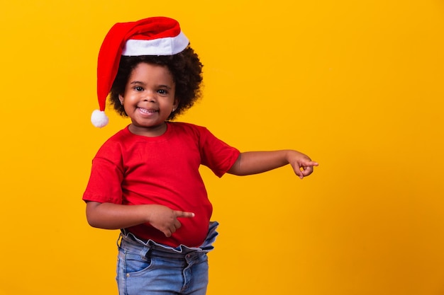 Petite fille afro en T-shirt rouge et bonnet de Noel habillé pour Noël avec un espace pour le texte pointant.