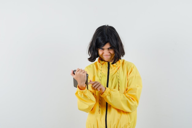 Petite fille à l'aide de la calculatrice en sweat à capuche jaune et à la recherche d'hésitant. vue de face.