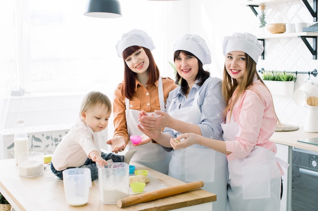 Petite fille aide à faire des cupcakes avec sa mère, sa tante et sa grand-mère. De jolies femmes sourient et s'amusent en cuisinant ensemble à la maison