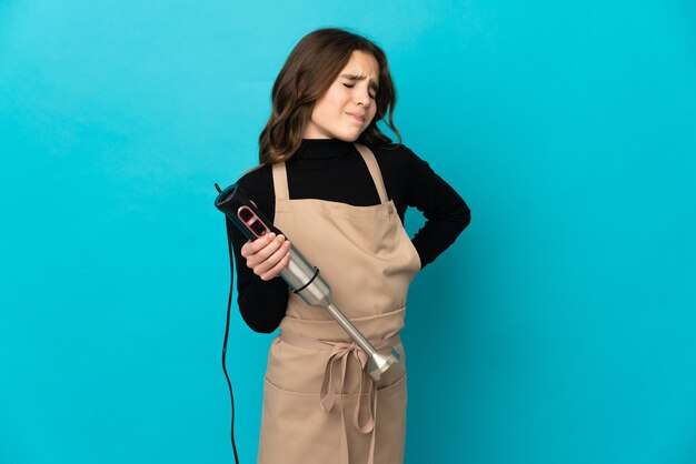 Petite fille à l'aide d'un mixeur plongeant isolé sur un mur bleu souffrant de maux de dos pour avoir fait un effort