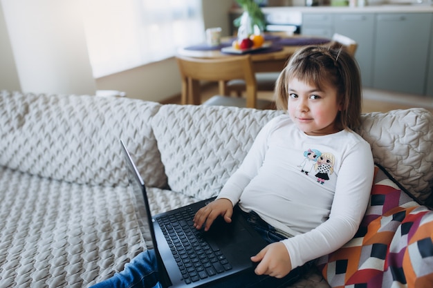 Petite fille à l'aide d'un ordinateur portable sur le canapé