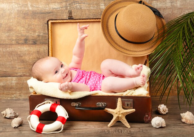 Petite fille allongée dans une valise avec des accessoires de plage sur fond marron