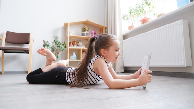 Petite fille allongée sur un plancher en bois avec un livre