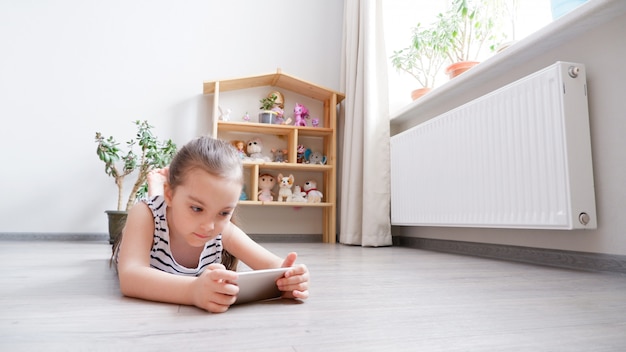 Petite fille allongée sur un plancher en bois avec un téléphone