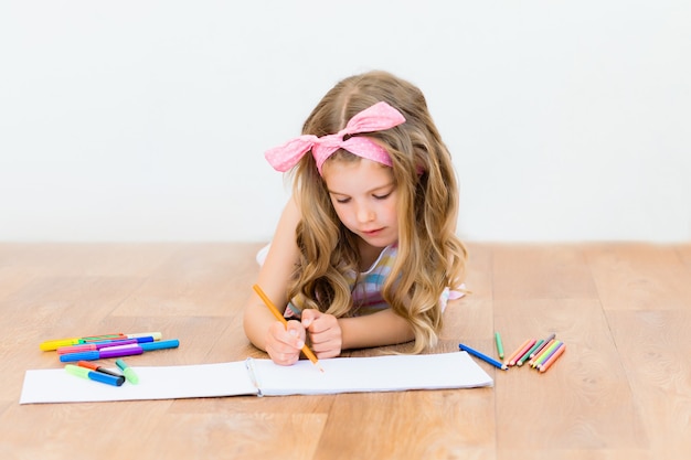 Petite fille allongée sur le sol dessine avec des crayons