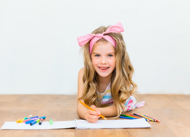 Petite fille allongée sur le sol dessine avec des crayons