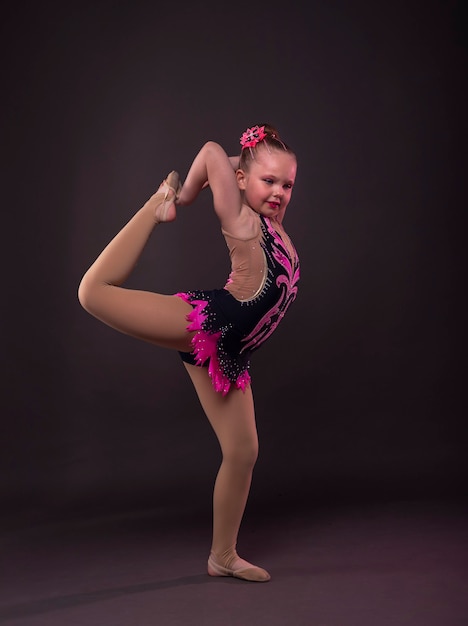 Petite fille amusante essayant de faire un cercle en costume de gymnaste noir et rose en studio.