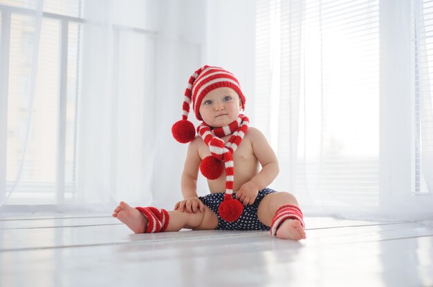 La petite fille d'un an au chapeau rouge est assise sur le fond d'une fenêtre.