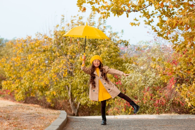 Une petite fille d'apparence asiatique tient un parapluie jaune en automne