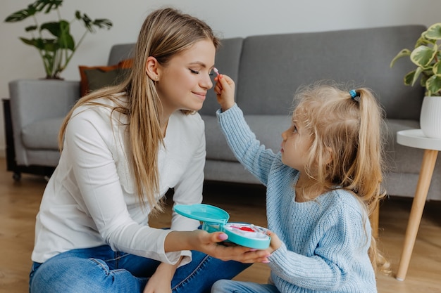 Petite fille appliquer le maquillage à la mère avec des produits cosmétiques jouets