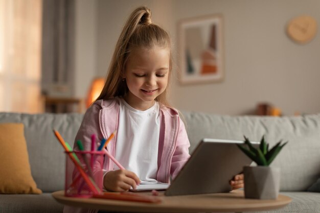 Petite fille apprenant à l'aide d'une tablette et prenant des notes à la maison