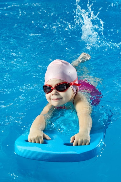 Petite fille apprenant à nager dans une piscine intérieure avec planche de billard