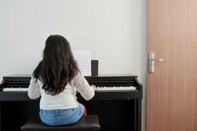 Petite fille apprenant la symphonie et jouant du piano à la maison, vue de dos