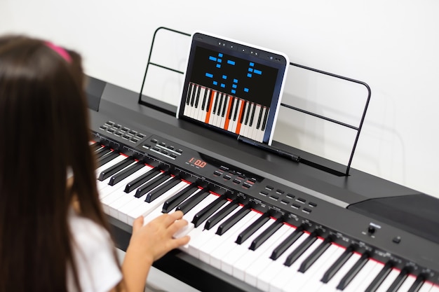 Une petite fille apprend à jouer du piano grâce à des leçons vidéo. Apprentissage à distance en ligne pendant covid-19