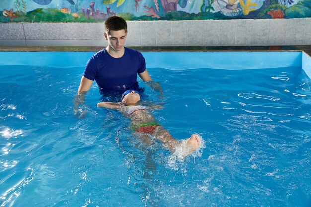 Une petite fille apprend à nager dans la piscine avec son professeur.